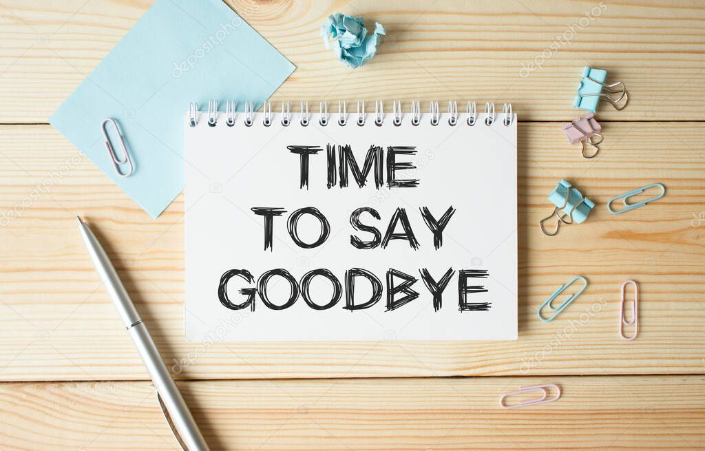 Time to say goodbye text. A concept that means a moment of separation from something. Notepad on a wooden table with a cup of coffee and glasses