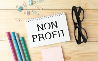 Kalemlerin, hesap makinesinin yanındaki masaüstündeki bir dizüstü bilgisayarda NON PROFIT metni