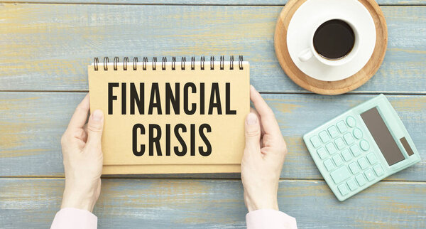 Text FINANCIAL CRISIS in notebook on wooden table with office tools.