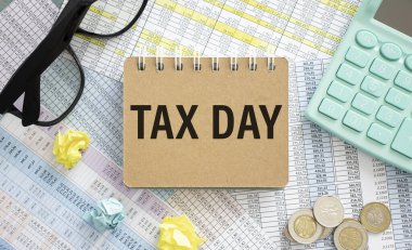 Finansal belgeleri ve ofis malzemelerini dağıtan bir defterde Vergi Günü metni.