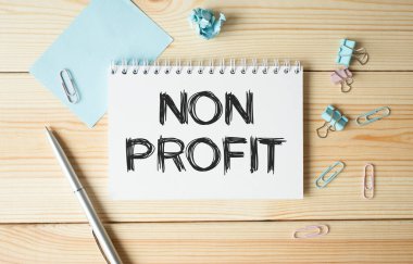 Tahta bir masanın üzerinde NON PROFIT yazılı bir ofis kağıdı var. Hesap makinesi, bardak, kalem, buruşuk kağıt ve bir fincan kahve ile iş yeri.