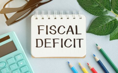 Notlar, hesap makinesi ve beyaz arkaplanda kum saati için FISCAL DEFICIT kağıdı yazılı beyaz kart. İş konsepti. Kahverengi arkaplan.