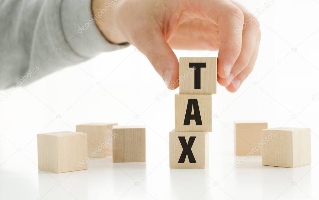 business man at the desk in the office Show a wooden cube with the word tax on corporate business investments.