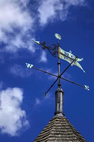 Weather vane on pointed roof against a blue sky