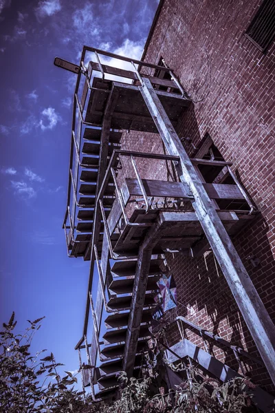 Rusty fire escape of derelict red brick building — Stock Photo, Image