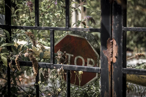 Decaying stop sign behind rusty metal gate — Stock Photo, Image