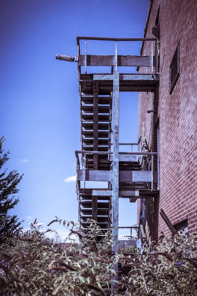 Rusty escada de incêndio de edifício tijolo vermelho abandonado — Fotografia de Stock