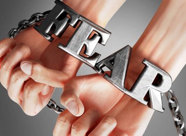 Fear restricting life and freedom, bringing enslavement, pain and misery to human life - symbolized by chains and shackles made of metal word Fear on a person's hands, 3d illustration