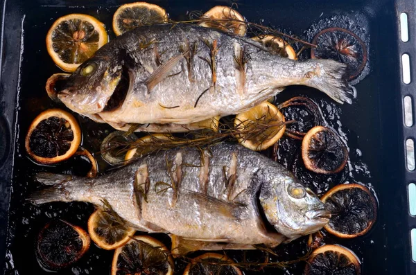 美味的烤了两条多头鱼 配上柠檬片 调味品和新鲜的迷迭香 放在黑色烤盘上 — 图库照片
