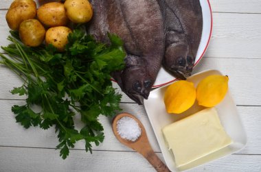 İki taze dil balığı, patates, tereyağı, maydanoz, limon, beyaz ahşap arka planda beyaz tabakta tuz. Uzayı kopyala Sole Meunire tarifi için İçindekiler