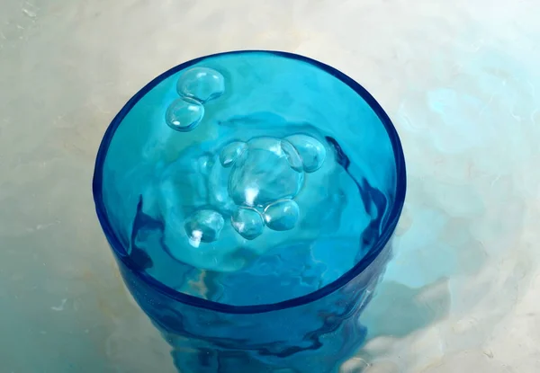 Overflowing water in a blue glass, full overflow glass with water and bubbles