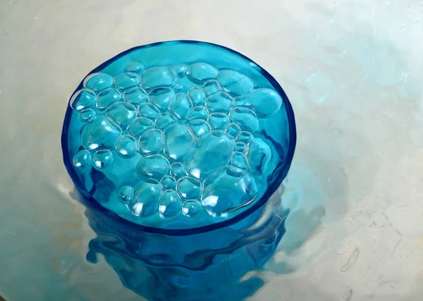 Overflowing water in a blue glass, full overflow glass with water and bubbles