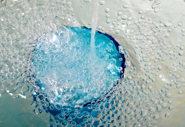 Overflowing water in a blue glass, full overflow glass with water and bubbles