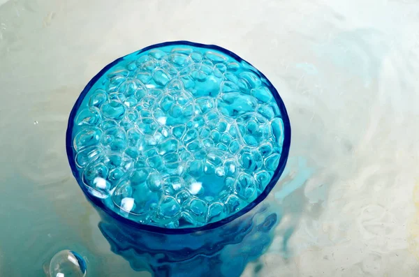 Mavi bardakta taşan su, su ve kabarcıklarla dolu bardaklar.