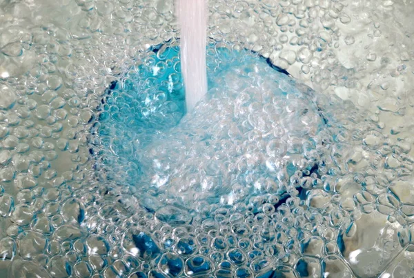 Overflowing water in a blue glass, full overflow glass with water and bubbles