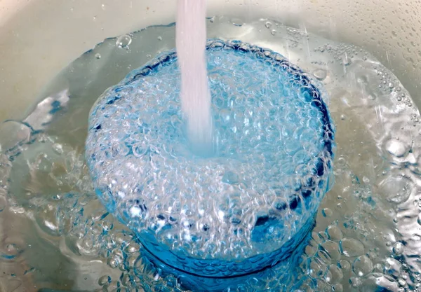 Overflowing water in a blue glass, full overflow glass with water and bubbles