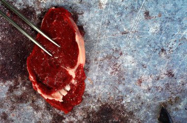 Kızarmış bıçak ve çatallı çiğ et, koyu kırsal arka planda biftek, üst manzara, kopyalama alanı