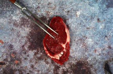 Kızarmış bıçak ve çatallı çiğ et, koyu kırsal arka planda biftek, üst manzara, kopyalama alanı