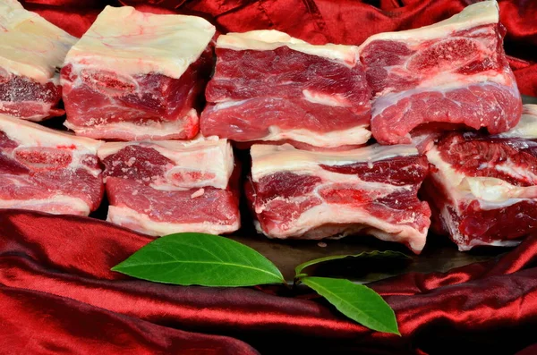 Siyah bir tabakta çiğ et kaburgası ve kırmızı ipek kumaştan bir arka plan. Çiğ Organik Biftek Kısa Kaburgaları