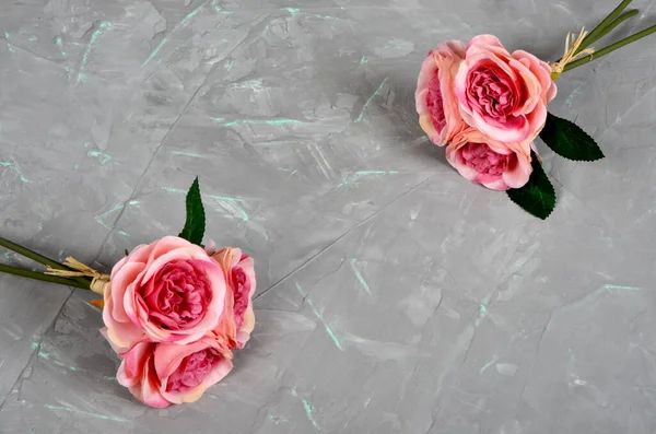 Two bouquets of pink roses on a gray cement wall with green veins