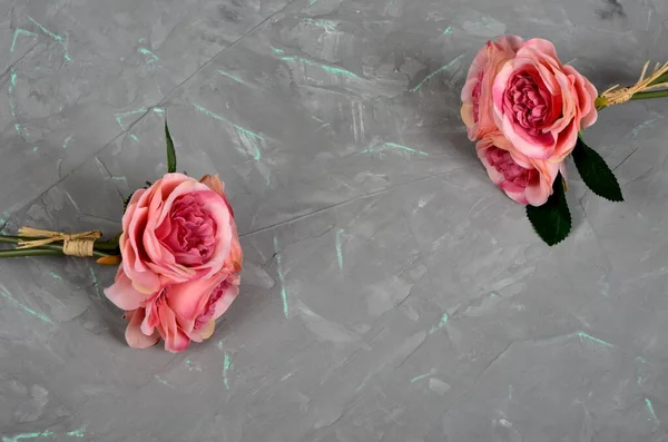 Two bouquets of pink roses on a gray cement wall with green veins