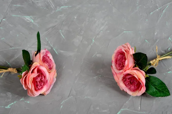 Two bouquets of pink roses on a gray cement wall with green veins