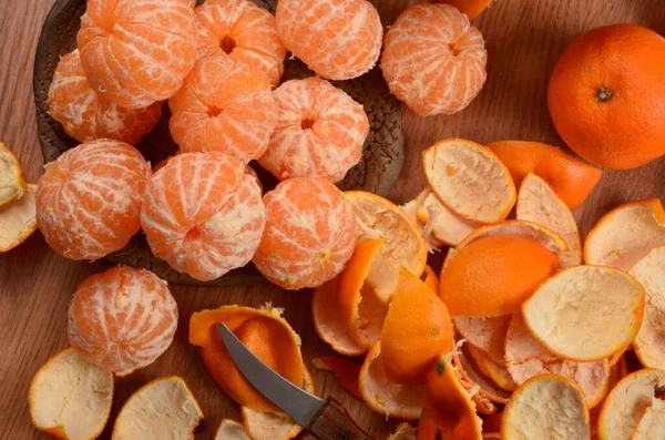 Ahşap bir arka planda kilden bir kasede taze soyulmuş mandalina ve mandalina kabuğu.