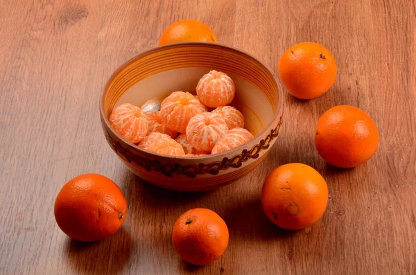 木の背景にある粘土製のボウルに新鮮な皮をむいたタンジェリン 新鮮なオレンジに囲まれて — ストック写真