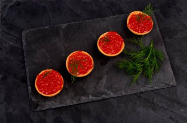 Siyah taş tabakta kırmızı somon havyarlı turta, yeşil dereotuyla süslenmiş, yakın plan. Uzayı kopyala Deniz ürünleri aperatifi