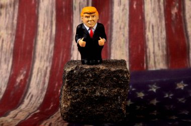 RIGA, LATVIA - HAZİRAN 07, 2021: Küçük Donald Trump figürü bir kayanın üzerinde duruyor, klasik ABD bayrak alanı