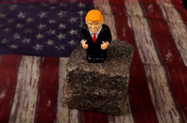 RIGA, LATVIA - HAZİRAN 07, 2021: Küçük Donald Trump figürü bir kayanın üzerinde duruyor, klasik ABD bayrak alanı