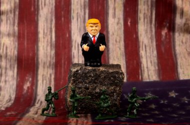 RIGA, LATVIA - HAZİRAN 07, 2021: Bir kayanın üzerinde duran küçük Donald Trump figürü, ayaklarının dibinde duran asker figürleri, klasik ABD bayrak alanı