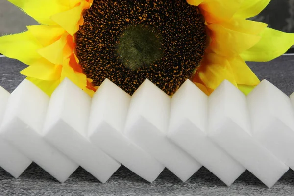 Gri arka planda melamin süngerleri, arka planda sarı ayçiçeği, mutfak ve ev temizliği araçları