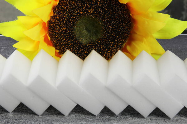 Губки меламина на сером фоне, желтый подсолнух на заднем плане, инструменты для кухни и уборки дома