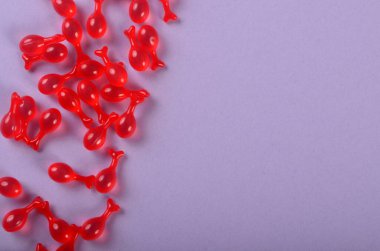 Mor arka planda kırmızı jelatin kapsüller var. Polipeptit Kapsül Havyarı Özü Sıvı İnce Çizgileri Parlatan Nemlendirici Cilt Bakımı