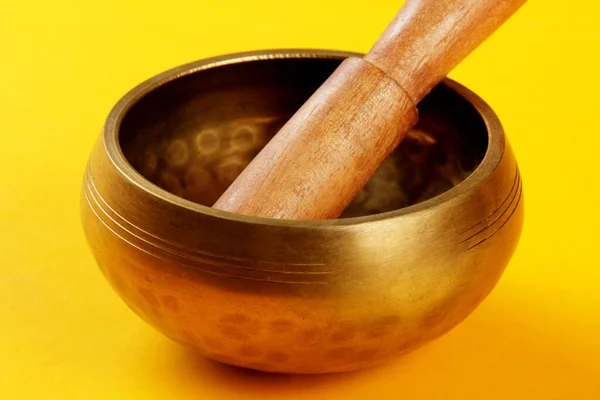 A Tibetan Singing Bowl with a wooden stick on a yellow background, green cloth