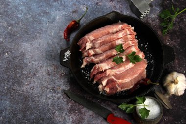 Çiğ domuz eti dilimleri, baharatlar ve siyah bir tavada otlar. Siyah arka plan. Metin için üst görünüm alanı