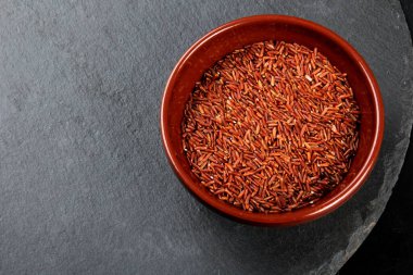 Siyah taş bir tabakta kil bir kasede çiğ kırmızı pirinç. Pişmemiş yabani pirinç, üst manzara.