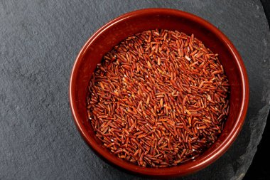 Siyah taş bir tabakta kil bir kasede çiğ kırmızı pirinç. Pişmemiş yabani pirinç, üst manzara.