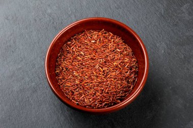 Siyah taş bir tabakta kil bir kasede çiğ kırmızı pirinç. Pişmemiş yabani pirinç, üst manzara.
