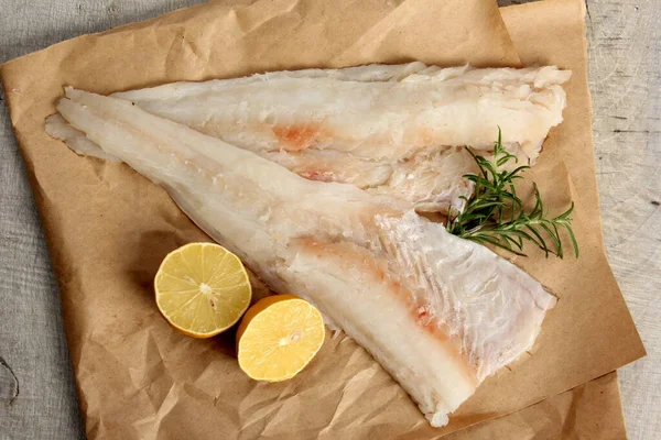 Two Piece of sea fish filet on a paper , decorated with lemon and rosemary, white raw fish filet without a skin