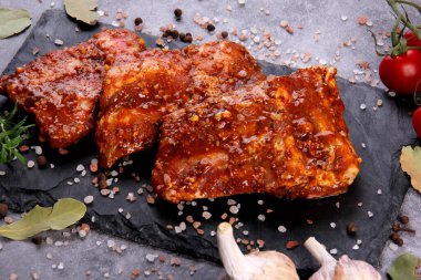 Çiğ domuz pirzolası, siyah taş tabakta pişirilmeye hazır. Çiğ bbq kaburga, ızgara için marine edilmiş et, kemikli et.