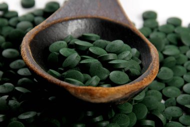 Ahşap bir kaşıkta yeşil Hughulina tabletleri. Sağlıklı süper gıda diyeti ve detoks beslenme konsepti 