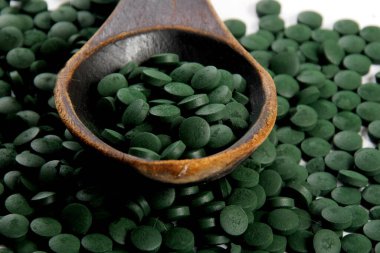 Ahşap bir kaşıkta yeşil Hughulina tabletleri. Sağlıklı süper gıda diyeti ve detoks beslenme konsepti 