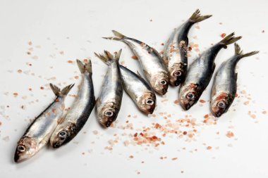 Beyaz bir zemin üzerinde pembe Himalaya tuzu bulunan taze çiğ Baltık ringası. Taze gümüş balık. 