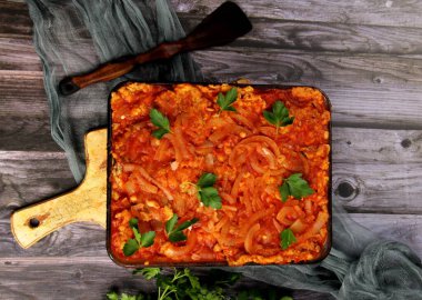 Domates soslu fırında balık ve cam kasede soğan. Domates soslu sebzeli balık. Koyu ahşap arka plan. Üst görünüm. 