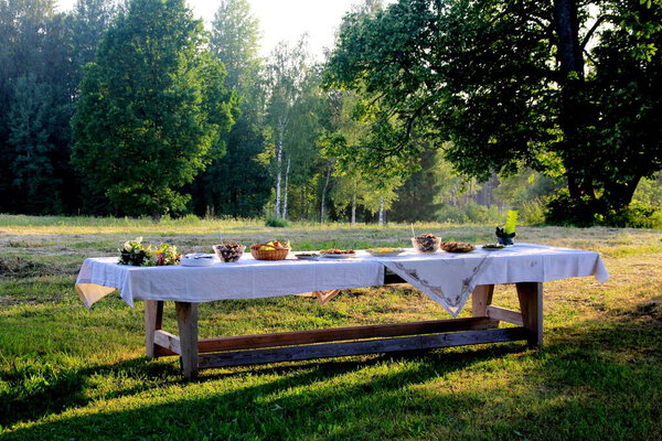 Giant wooden picnic table in scenic park with old trees, yellow sunset light. Outdoor Table food lunch concept