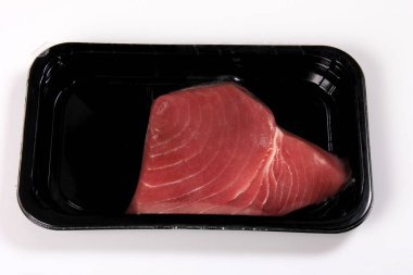 raw tuna steak in black vacuum package isolated on white background, top view
