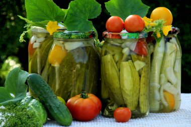 Preserves vegetables in glass jars on the table in summer garden. glass jars with various vegetables. Marinated food.Jars of pickled vegetables in the garden.