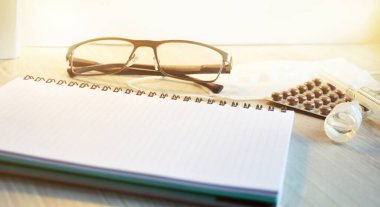 Beyaz tabletli, kalemli, gözlüklü ve haplı tıbbi masaüstü.